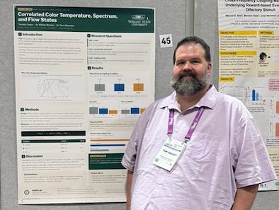 A man stands in front of a poster at a research conference.